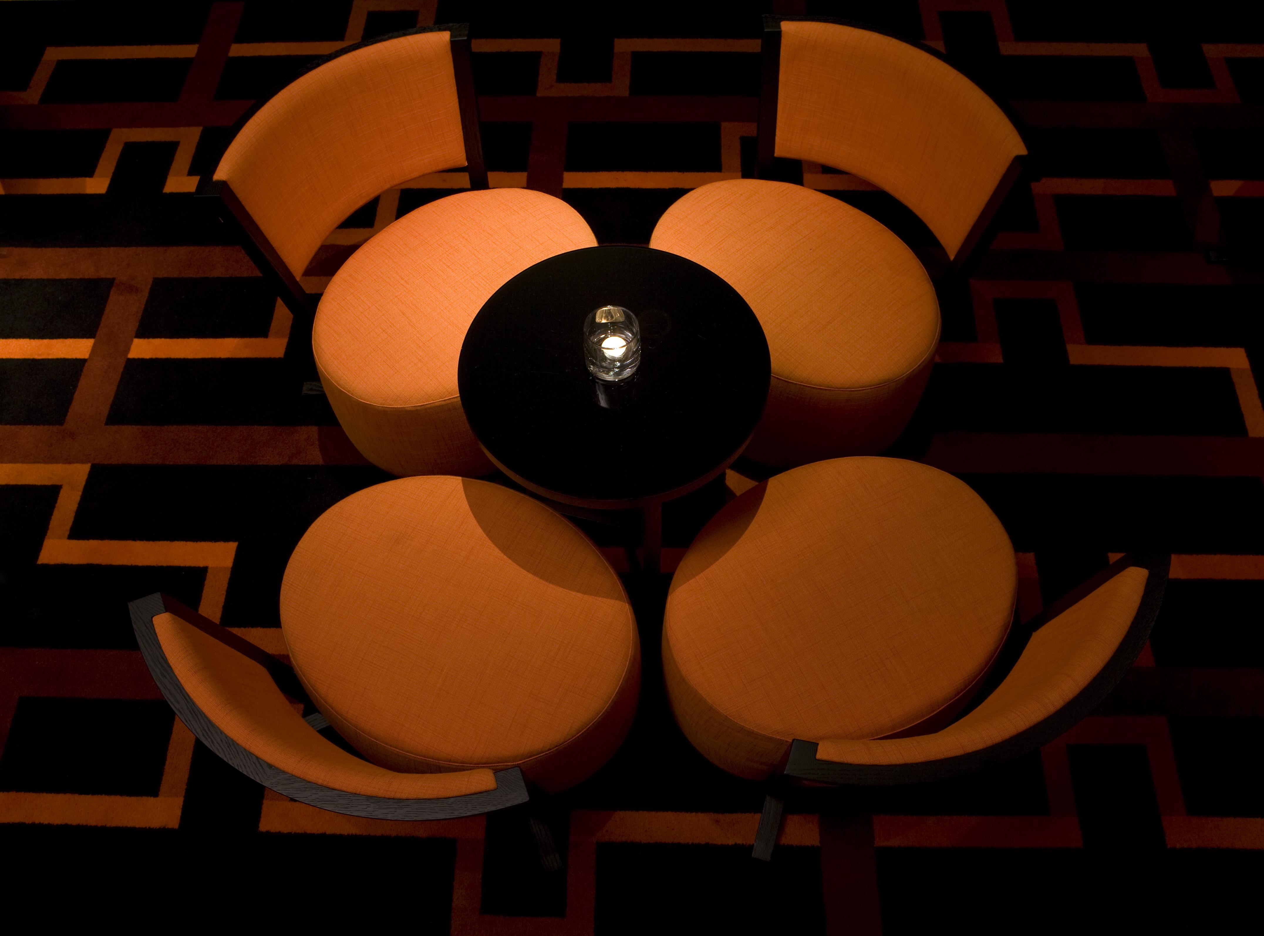 The Fitzwilliam Hotel Белфаст Екстериор снимка The image shows a small seating arrangement consisting of four orange chairs arranged around a circular black table. The setting appears to be in a dimly lit area, emphasizing the warm tones of the chairs and the dark finish of the table. The floor d