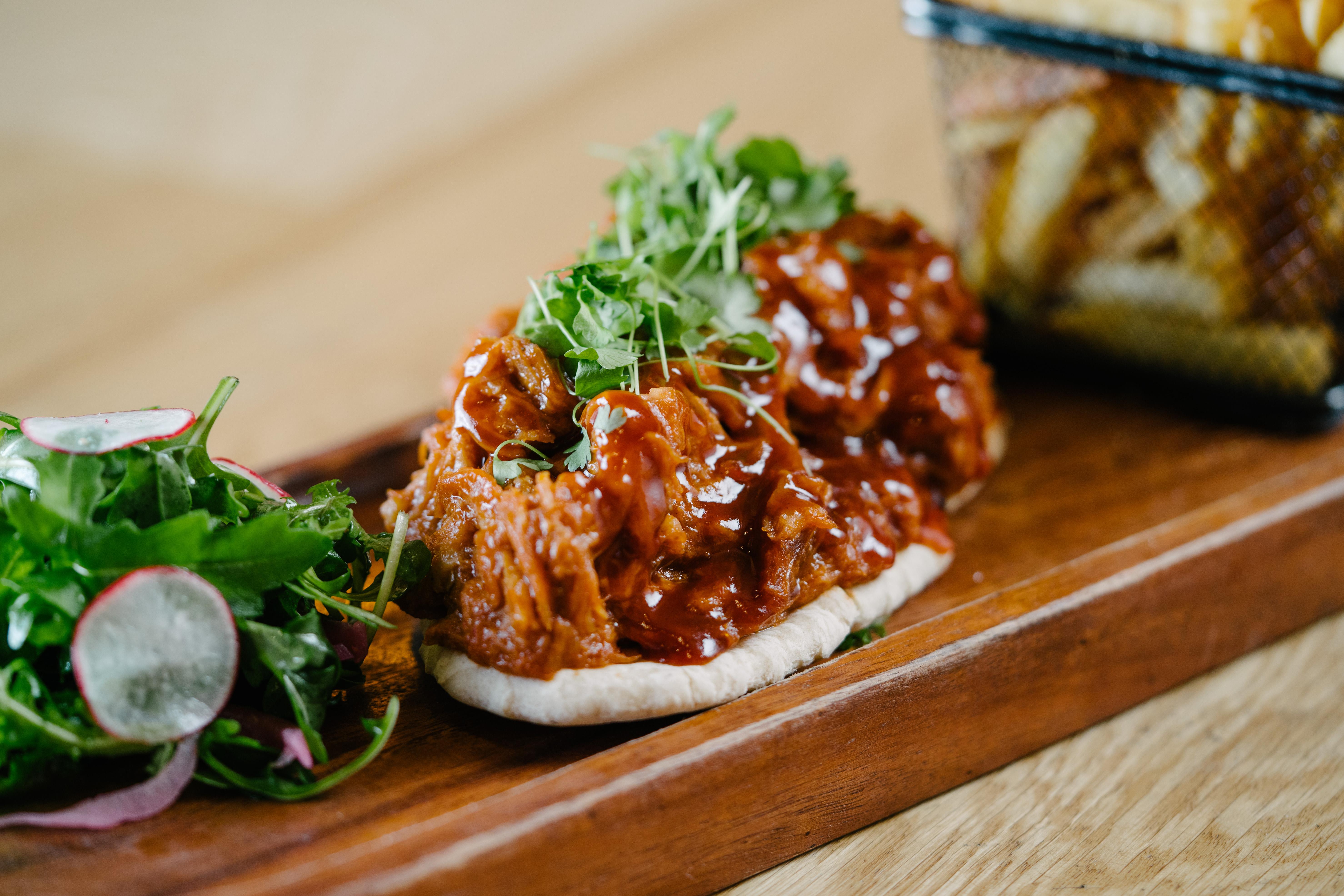 The Fitzwilliam Hotel Белфаст Екстериор снимка The photo shows a wooden platter featuring two pieces of bread topped with pulled meat covered in a rich barbecue sauce. The dish is garnished with fresh greens, including sprouts. On the side, there is a small serving of mixed salad with radishes an